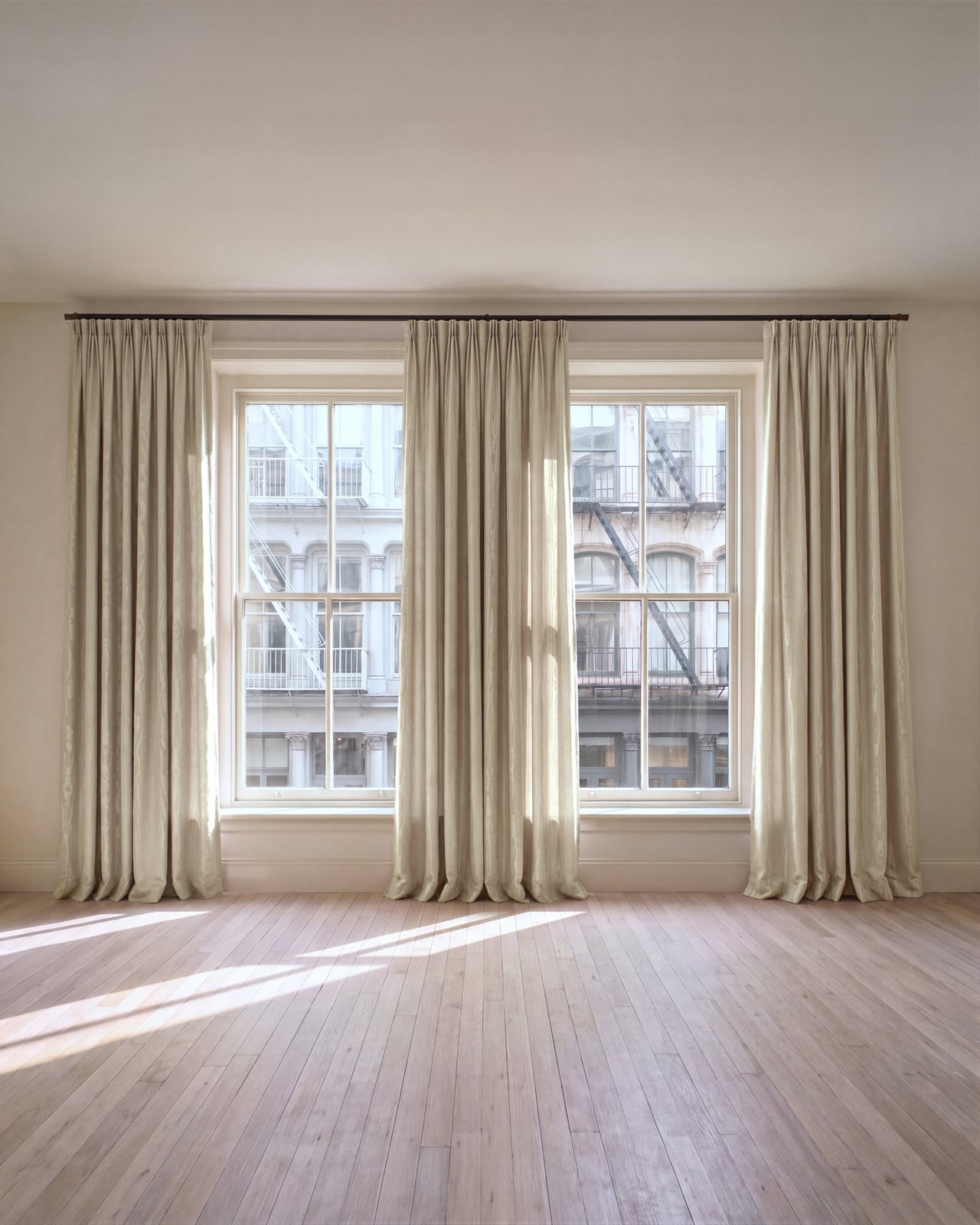 The Moire curtain in Sand hanging in soft folds across two windows above a wooden floor.