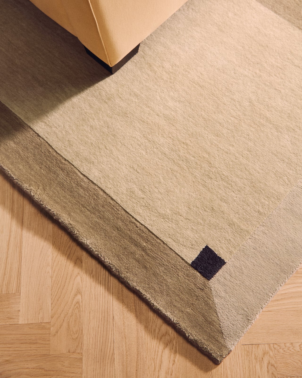 Parchment in Sand featuring a geometric panel pattern with contrasting dark corner accents and a smooth wool surface.
