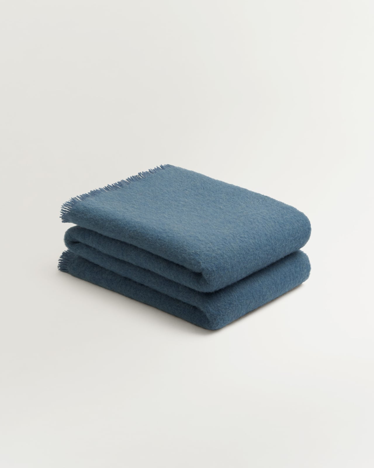 Solid Brushed Alpaca Throw in Slate Blue, ein denimblaues Wollplaid mit weicher Oberfläche und Fransen.