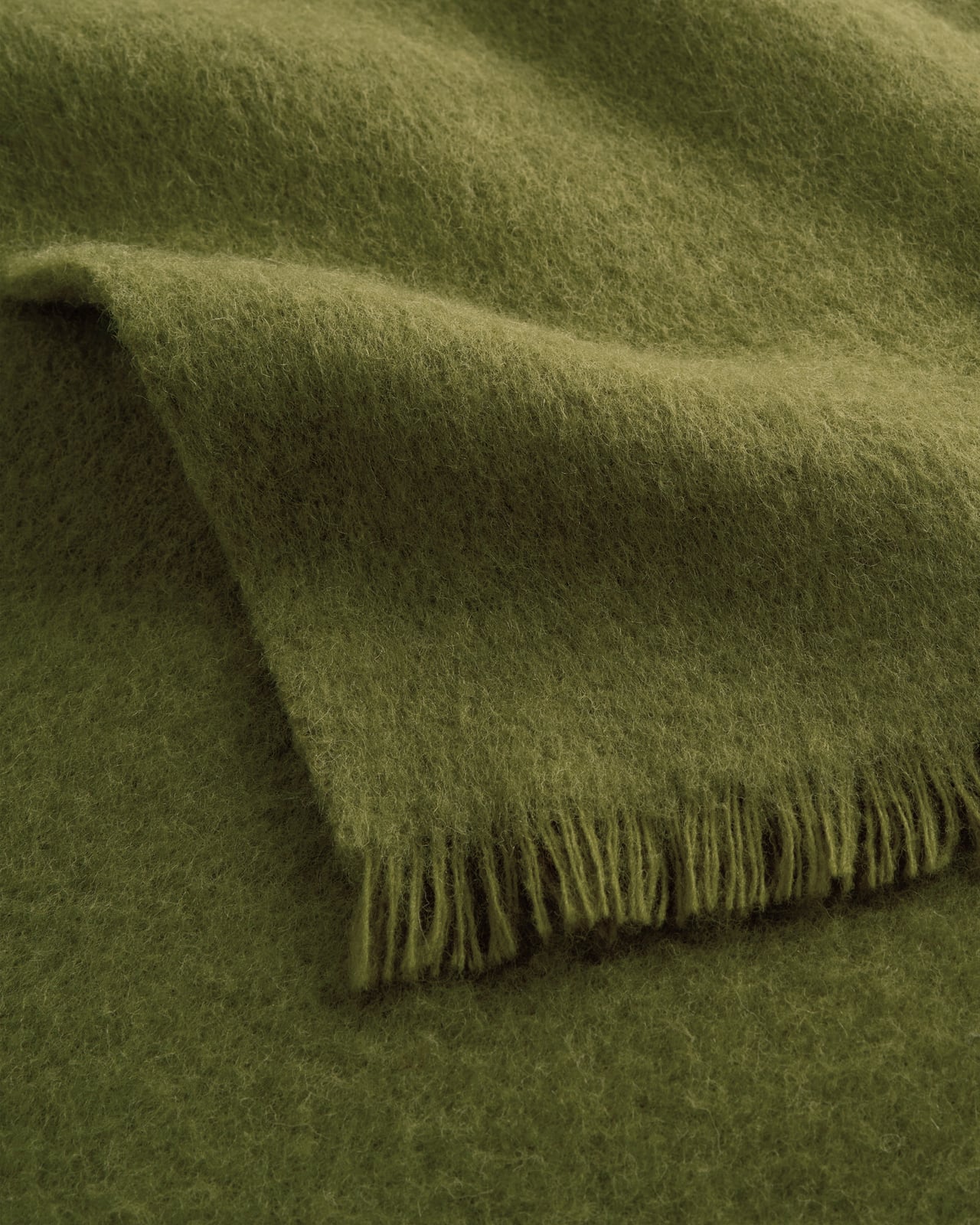 Solid Brushed Alpaca Throw i Milano Green, en klar olivgrön ull- och alpackapläd med borstad yta och fransar.