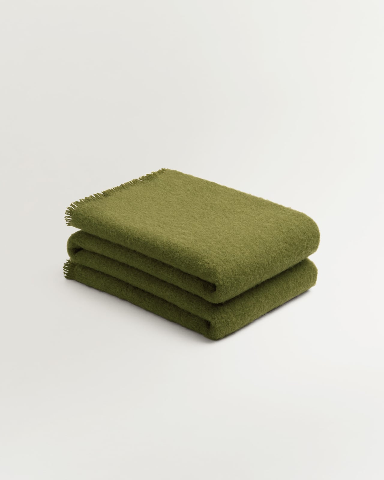 Solid Brushed Alpaca Throw i Milano Green, en klar olivgrön ull- och alpackapläd med borstad yta och fransar.