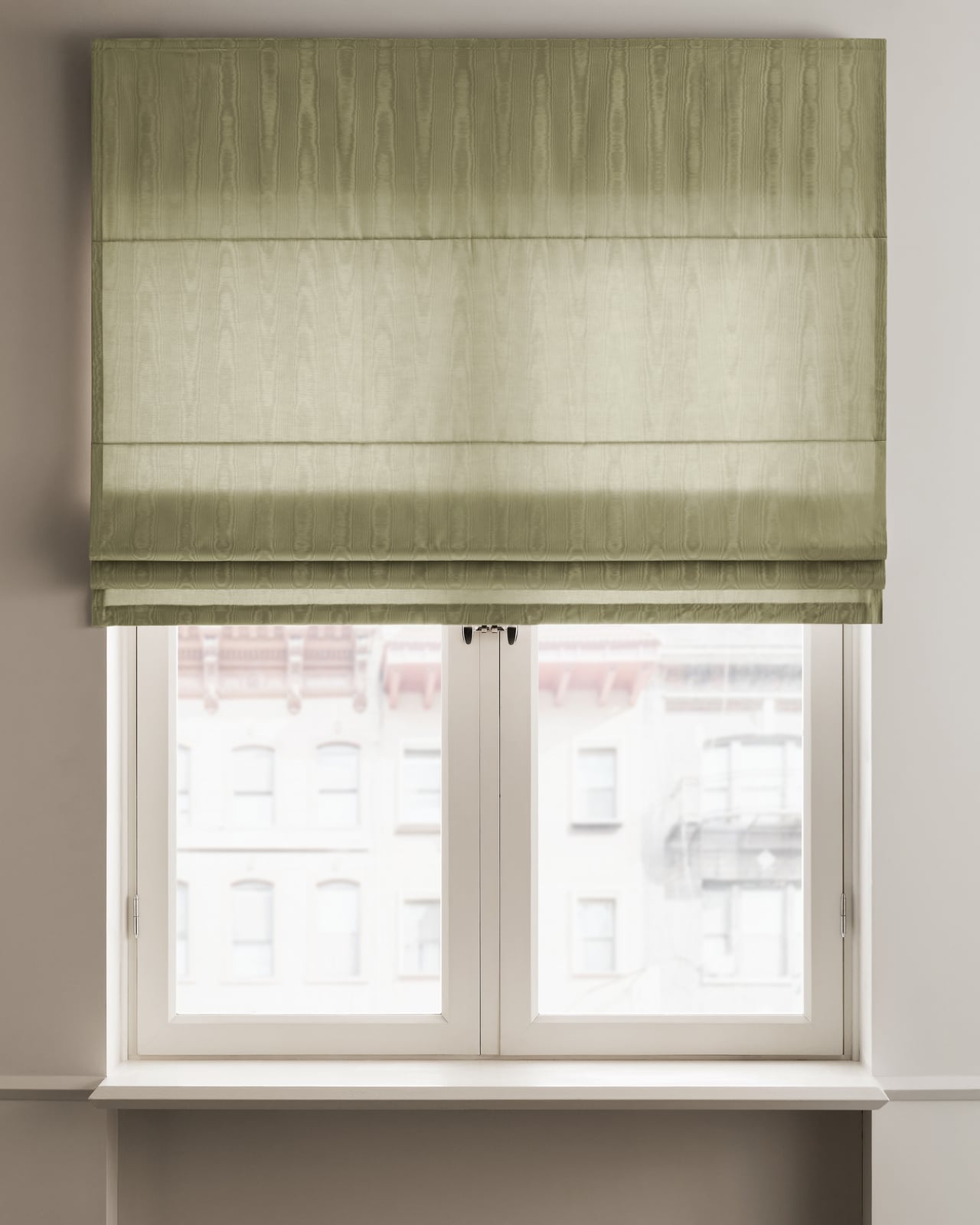 The Moire Roman Shade in Pistachio, mounted above a window with a delicate, water-like moire pattern catching the light.