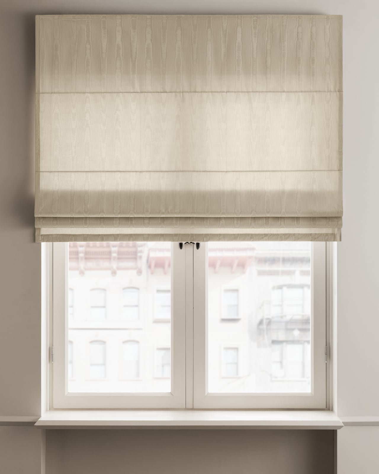 The Moire Roman Shade in Sand, shown mounted over a window with soft natural light highlighting its shifting moiré pattern.