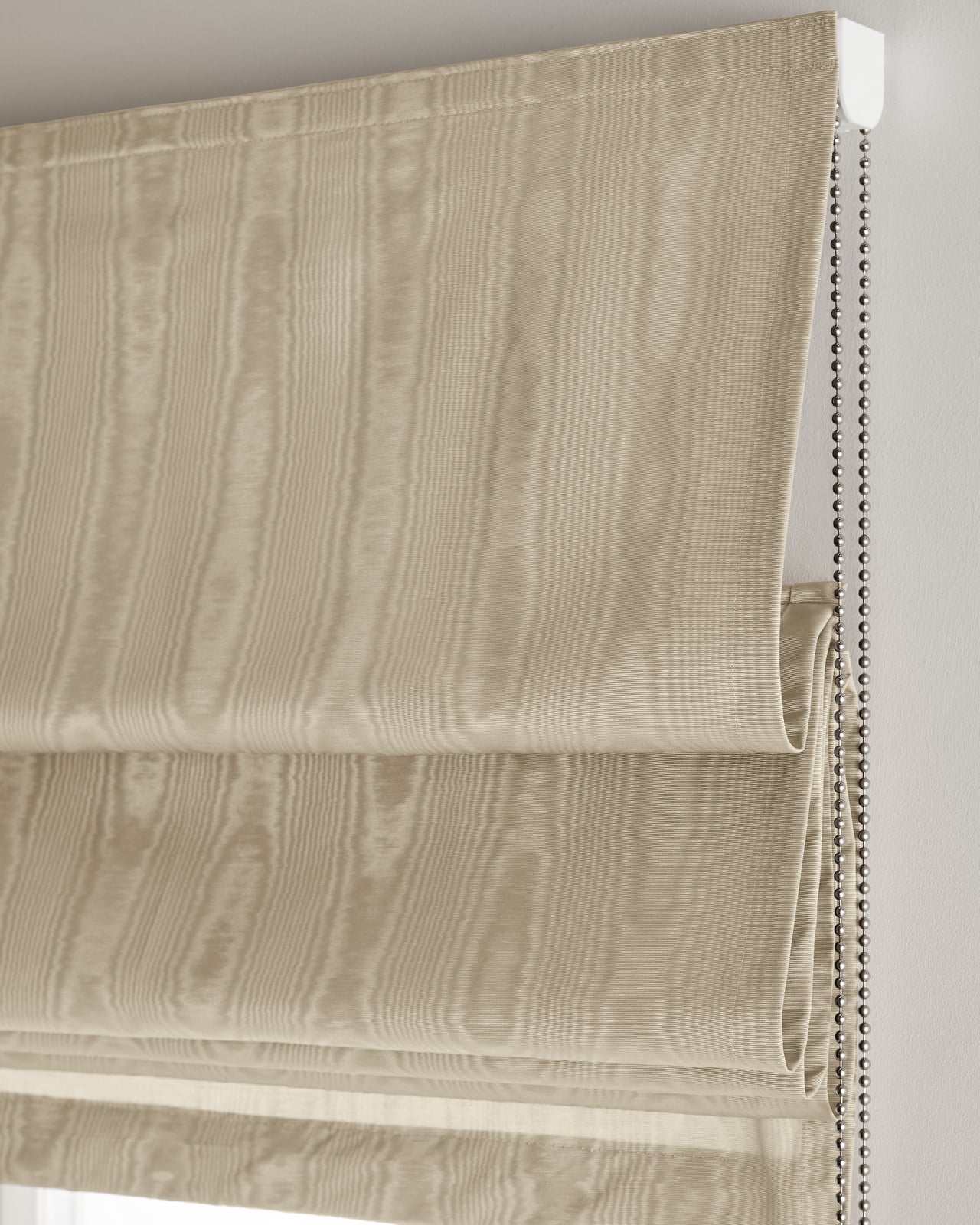 The Moire Roman Shade in Sand shown mounted over a window, highlighting its shifting water-like ripples in a warm cream tone.