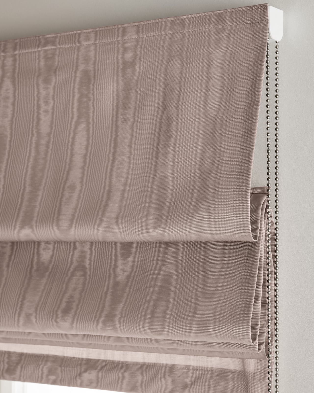 The Moire Roman Shade in Lavender shown mounted over a window, highlighting its fluid moire pattern in a muted purple tone.