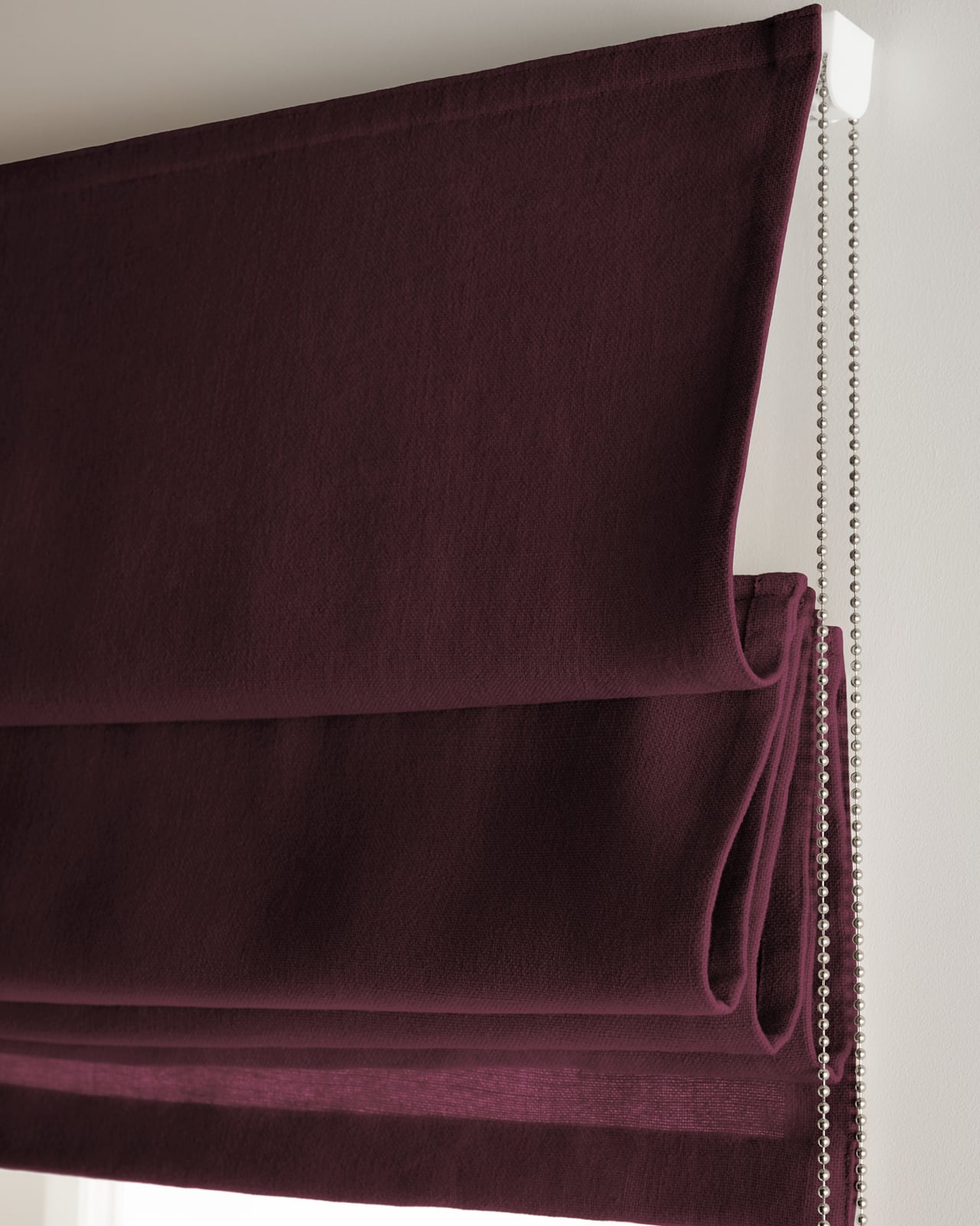 The Studio Linen Roman Shade in Deep Wine mounted over a window, highlighting its linen texture and rich tone.
