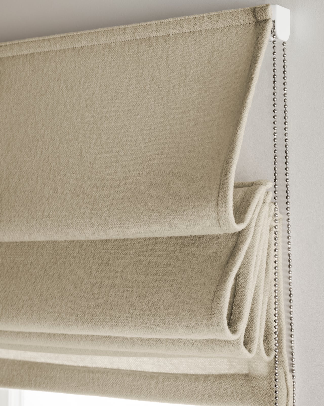 The Shelter Roman Shade - Blackout Lining - Sand shown over a window, highlighting its boiled wool fabric and soft beige tone.