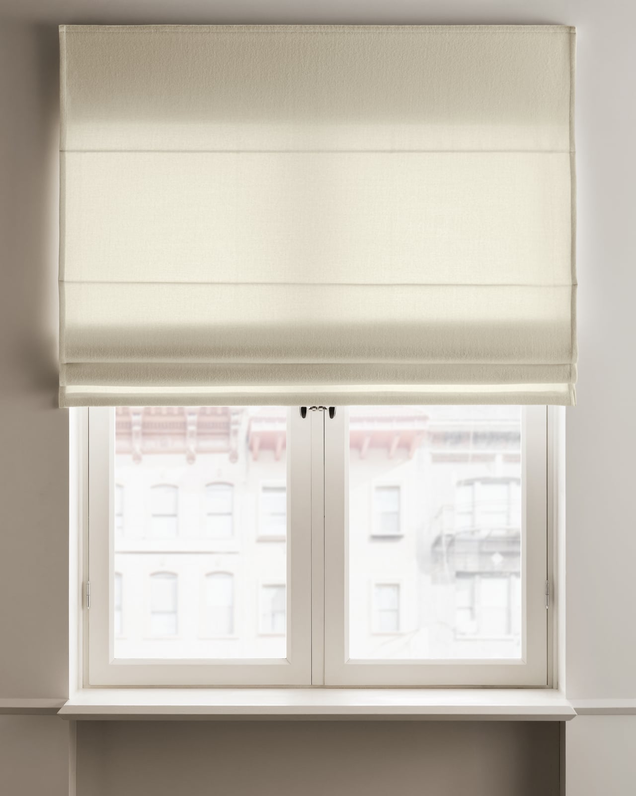 The Shelter Roman Shade in Warm White mounted over a window, showing its soft felted wool texture and clean horizontal folds.