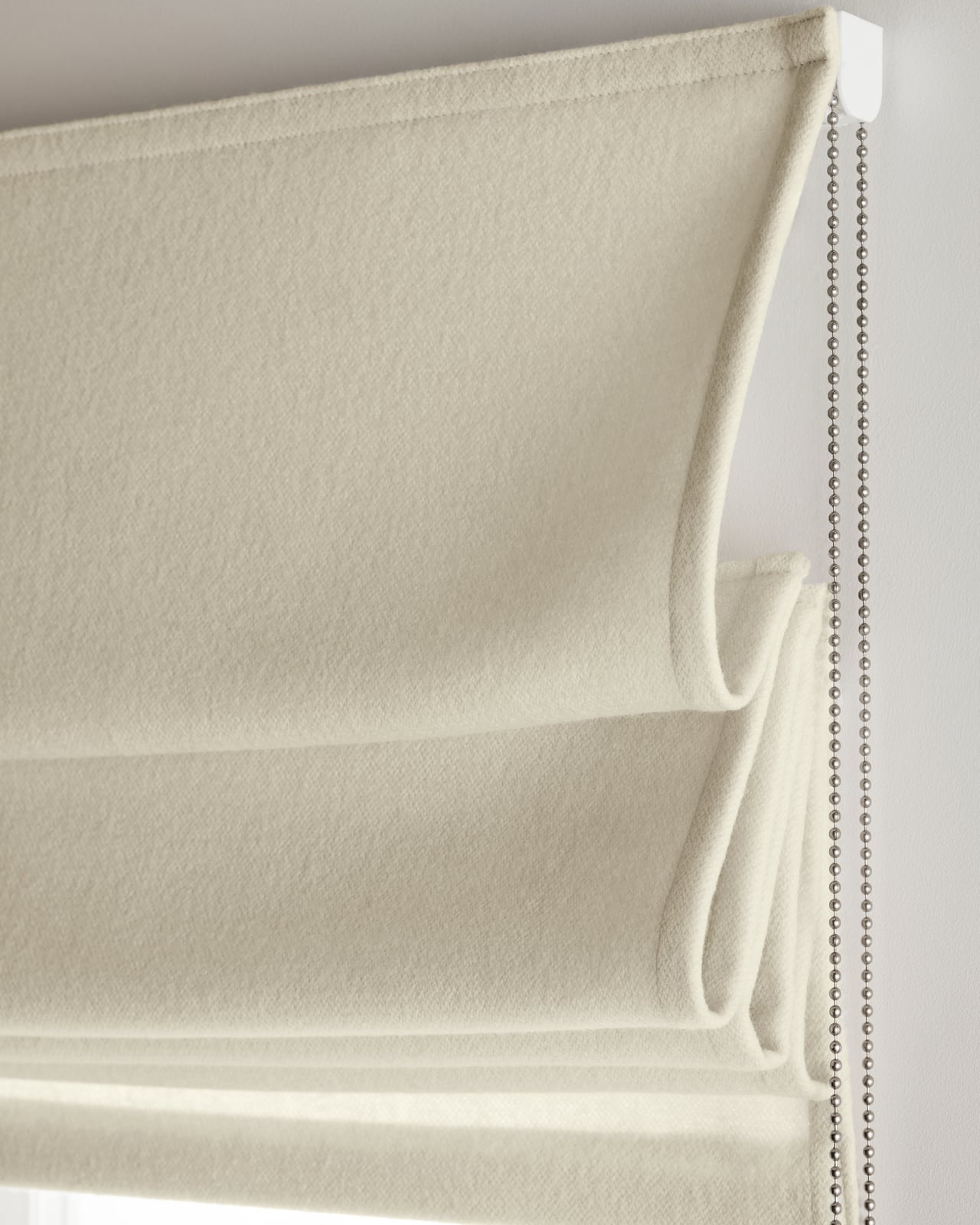 The Shelter Roman Shade in Warm White mounted over a window, highlighting its boiled wool texture.
