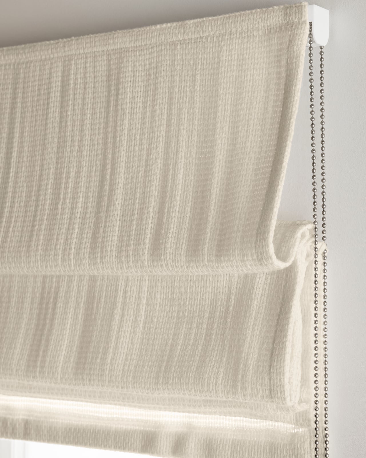 The Basket Weave Roman Shade in Perfect White, shown mounted over a window in a bright interior.